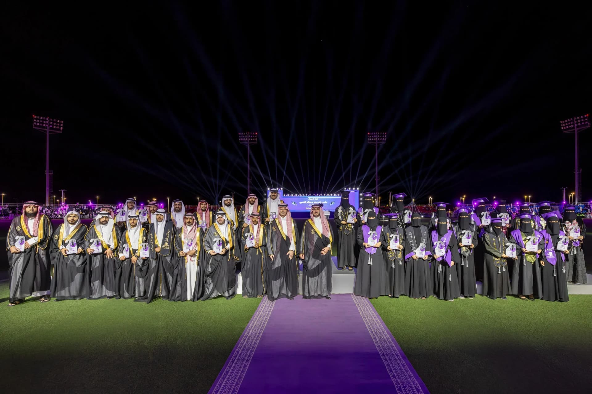 Al Jouf University graduation, female graduates on the field, dignitary seating, male graduates in traditional dress