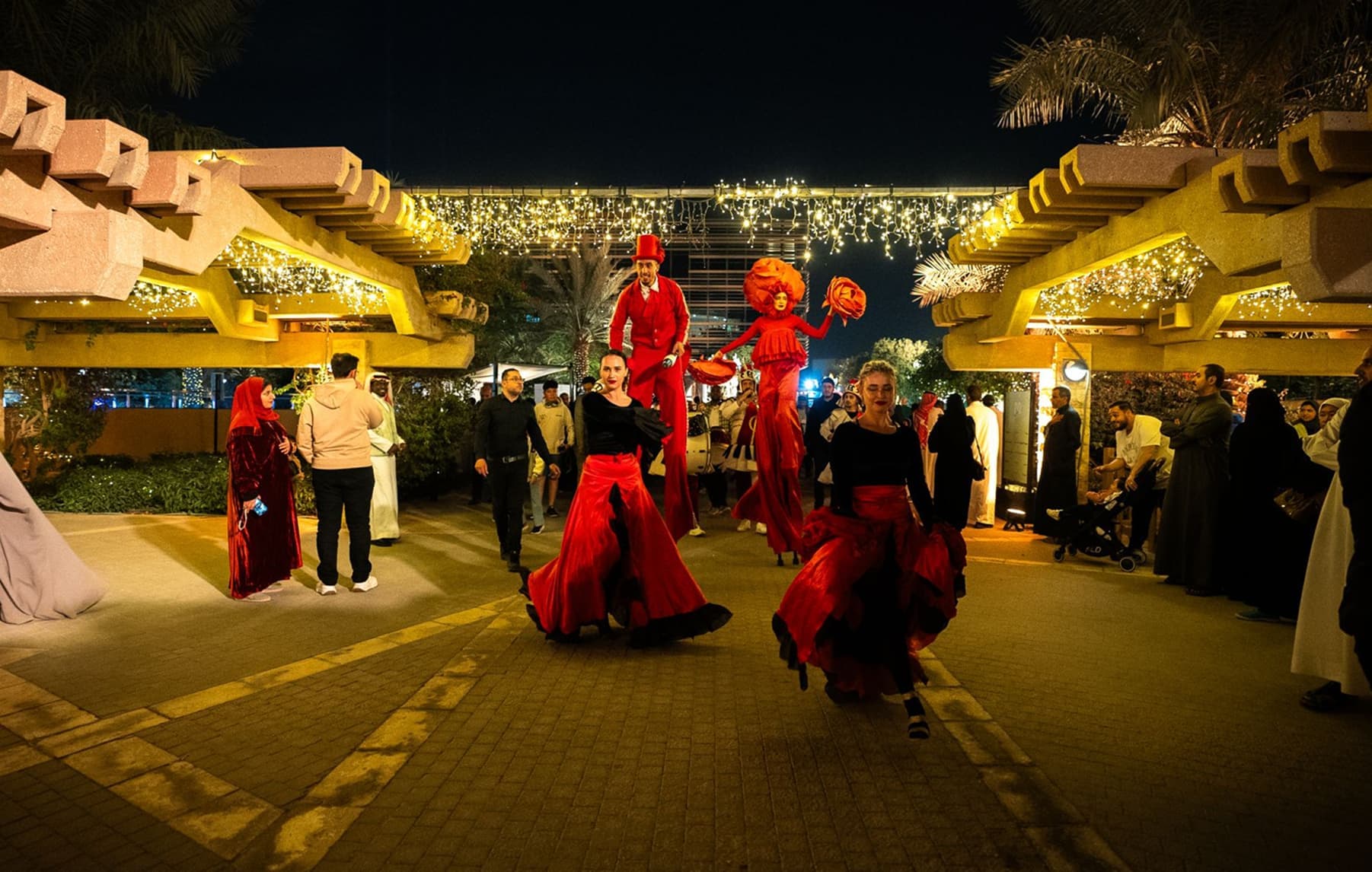 DQ Market, stilt performers at night, DQ branded community courtyard, illuminated wing performance