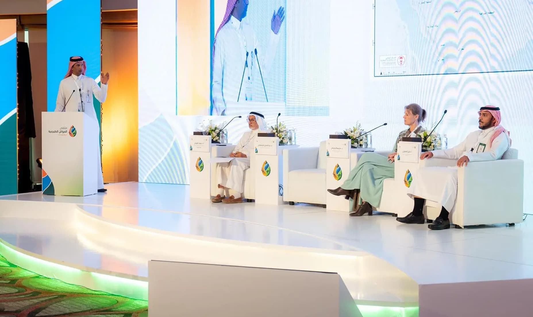 Natural Habitats Forum — speaker at branded podium, panel on stage with screen, speaker at podium